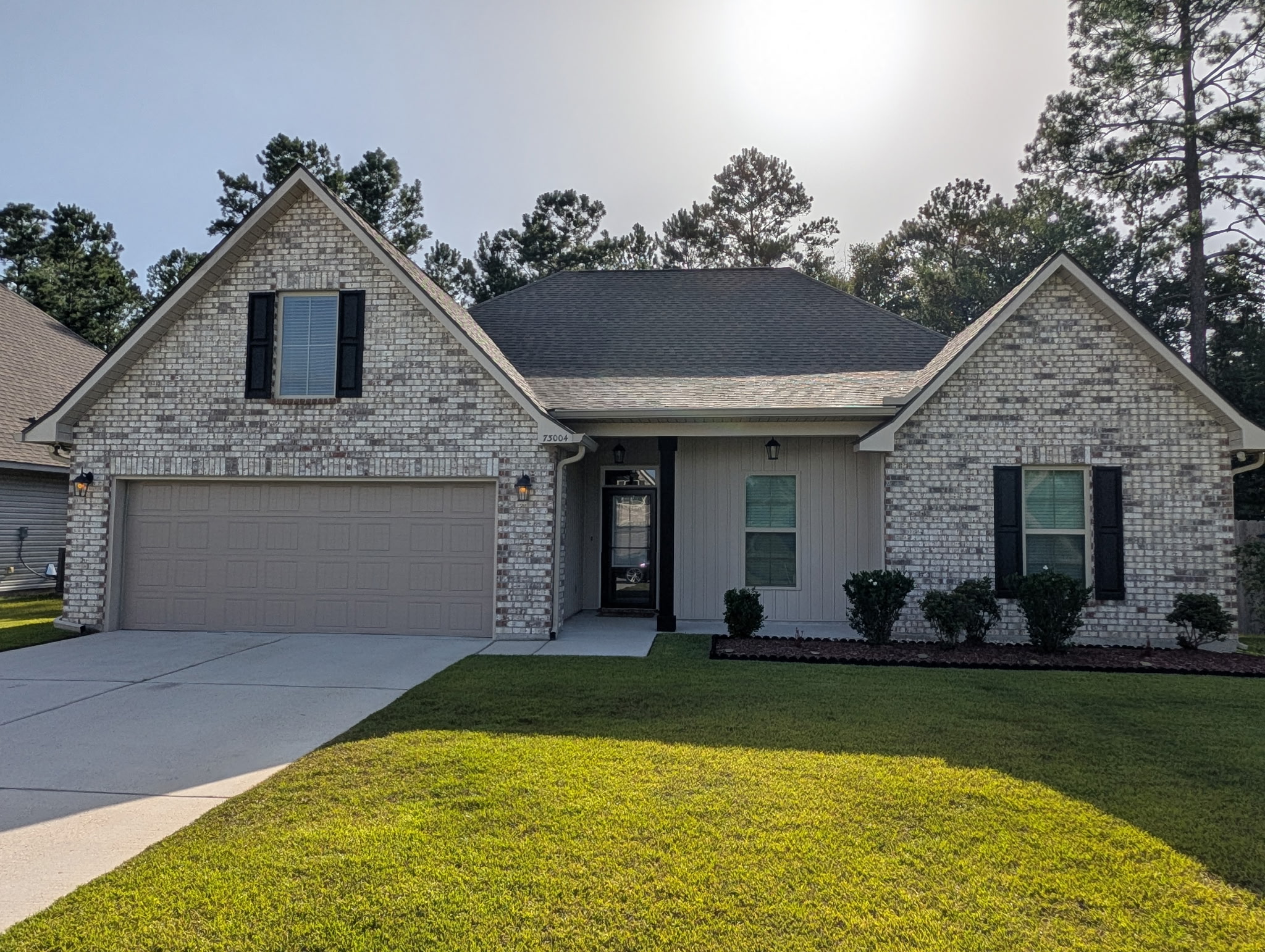 Light brick home with twin gables, dark shutters, and a landscaped front lawn
