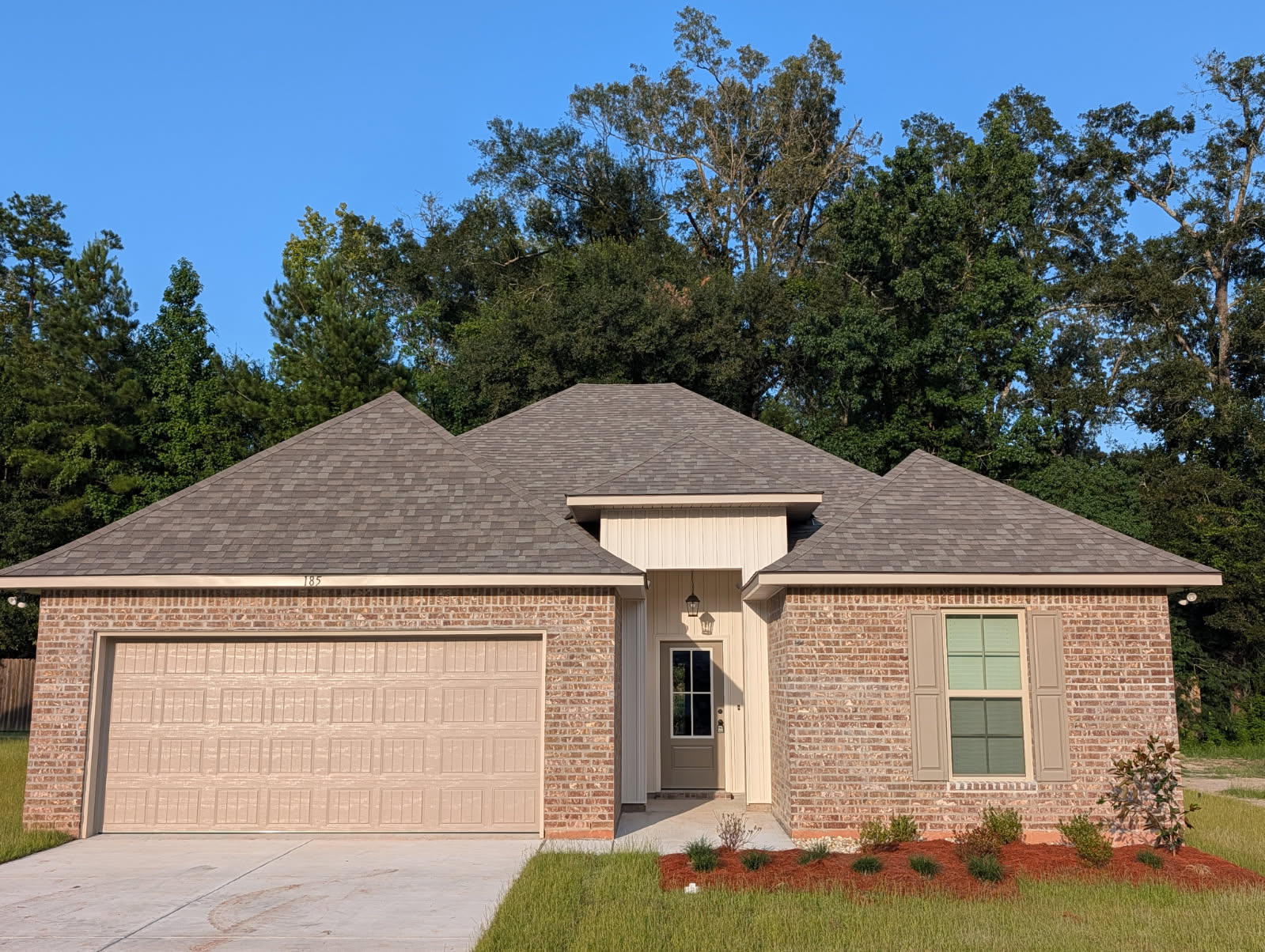 Single-story brick home with a two-car garage and wooded backdrop